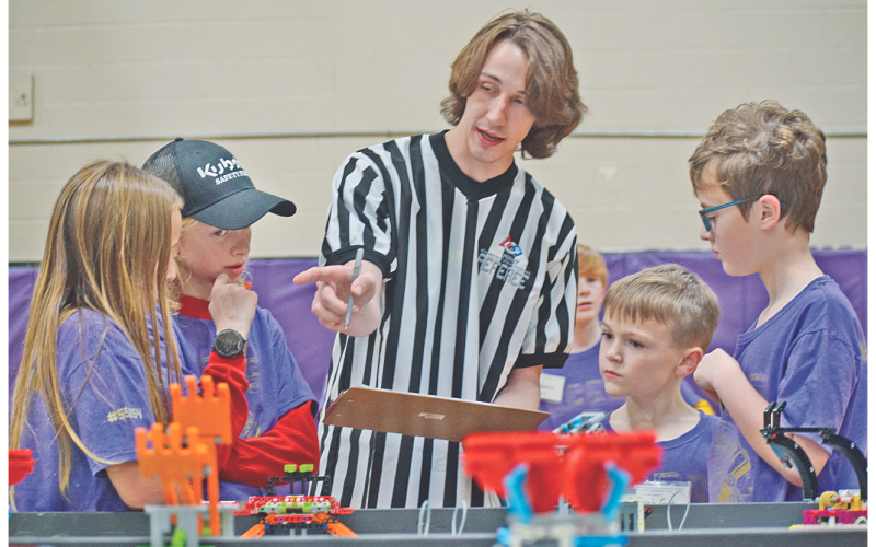 Members of the Bright Chickens of Lumpkin County Elementary School, from left, Chloe Fulton, Liam Alhadeff, Jacob Gee and Jacob Giles gather around First LEGO League referee Liam Orton as he explains the scoring process at Saturday’s competition.