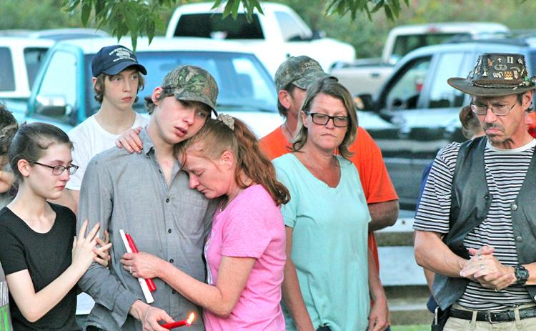 Austin Bender holds a candle in honor of his sister as he consoles his mother Carol Gillreath at last week’s vigil on Lake Zwerner.