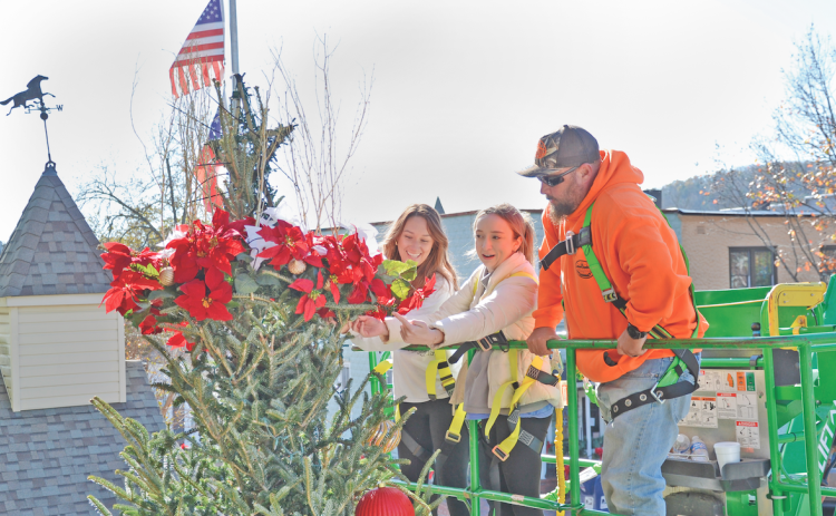 Skyler Alexander (left) and Ariel Alexander from City Hall and Jeremy Tanner from the City Works Department attach the wreath on the Christmas tree on the square.