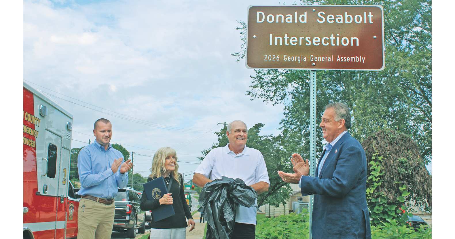 Retired Dahlonega-Lumpkin County Emergency Management Agency Director Donald Seabolt was all smiles Monday as a new sign was unveiled declaring the intersection of Pinetree Way and Morrison Moore Parkway the “Donald Seabolt Intersection.” Pictured from left are County Chairman Rhett Stringer, Gail Seabolt, Donald Seabolt and State Senator Steve Gooch.
