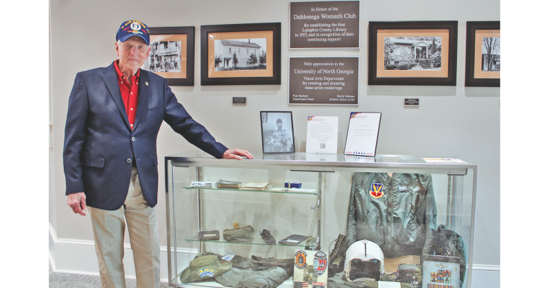 LTC Colonel (RET) Lewis “Lew” M. Houser is currently featured in a rotating exhibit at the Lumpkin County Library called “Outpost Alpha,” which honors local veterans. Here, he stands next to a glass case displaying Vietnam-era military memorabilia, including his Air Force flight jacket, helmet, gloves and service medals.