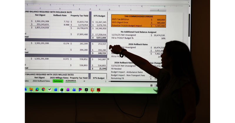 Lumpkin County Finance Director Abby Branan points at a slide in her 2027 budget presentation. The financial impact of errors in the 2025 property tax calculation can be seen at the upper right.