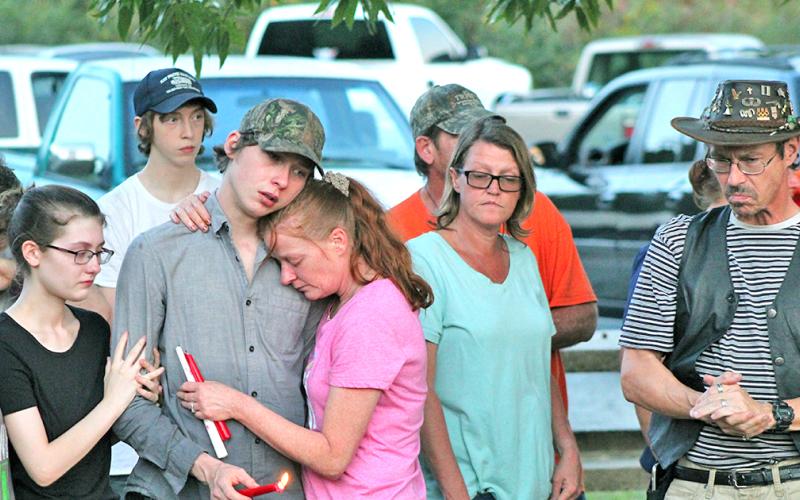 Austin Bender holds a candle in honor of his sister as he consoles his mother Carol Gillreath at last week’s vigil on Lake Zwerner.