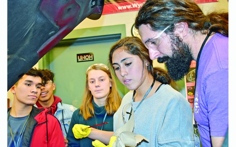 Jesse Perethian, LCHS graduate and now a bus driver for the school system, instructs Hope Kenney on how to check the oil in a vehicle while fellow students look on. This was just one of the lessons learned at the auto maintenance station during Senior Adulting Day.