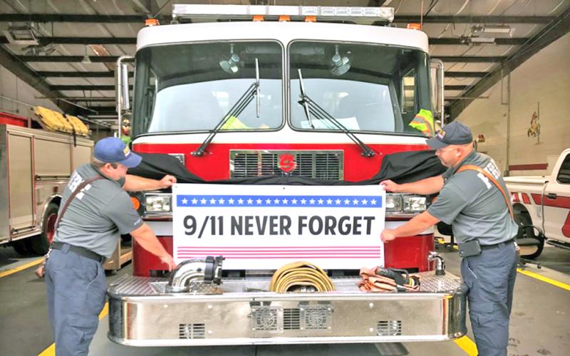 Firefighters/EMTs (from left) Jordan Dingess and Jody Holland from the Lumpkin County Fire Department check the fit of a banner that will be used for the 9/11 20th Anniversary Commemoration event on September 11, on the west end of the Gold Museum in downtown Dahlonega. The fire truck will be parked in front of Woody’s Barber Shop.