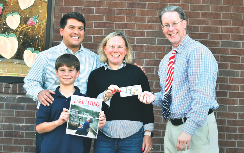 Jonathon, Sarah, and Jonathon Barge Jr., who goes by “J,” are all smiles having learned that Jonathon Barge won the Winter 2022 Lake Living cover contest for the picture of “J” in the family’s 1972 Alumacraft fishing boat “catching snowflakes instead of fish” on Lake Burton in January 2022. Enoch Autry, publisher of The Clayton Tribune in Rabun County, right, hands the family the $100 prize for winning the contest. (Photo by Megan Broome)