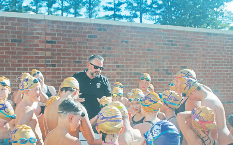 Lumpkin County Coach Jesse Turk leads the young swimmers in a chant before the team dove into the competition.
