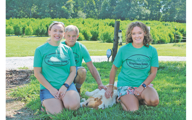 Pictured, from left, Lacey White, Bruce White, Barney the dog and Kelly White enjoy a shady patch of grass on the White Family Barn Farm.