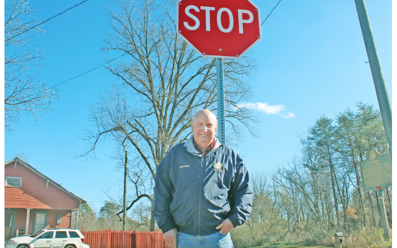 Lumpkin County Special Projects Manager Charles Trammell stands at the intersection of Castleberry Bridge Rd. and Auraria Rd., next to one of 11 flashing stop signs in the county.