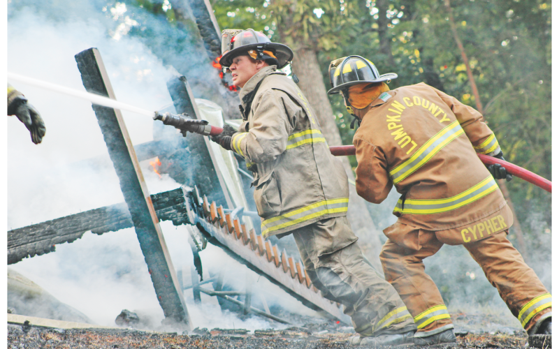 Lumpkin County firefighters Paul Northop, left, and Jean-Luc Cypher work to contain a quickly-spreading fire that ultimately claimed a Trahlyta Estates home last Friday.
