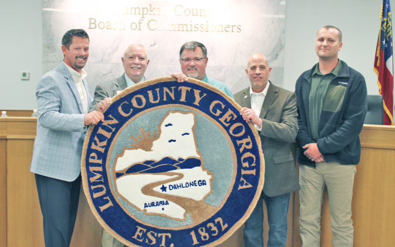 Chairman Chris Dockery (center) holds up a custom rug modeled after the Lumpkin County seal during his final meeting with the Board of Commissioners. The rug was a parting gift from fellow commissioners (from left) Tucker Greene, Dr. Bobby Mayfield, Jeff Moran and Rhett Stringer.