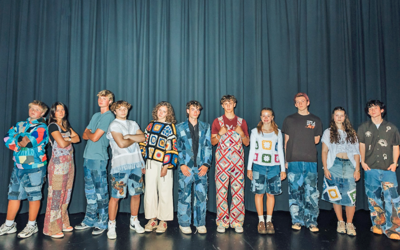 Junior Jeb Jackson (center) is flanked by 10 student models wearing his clothing brand, One Fifty Three Designs, during a charity fashion show held last month in the high school auditorium.