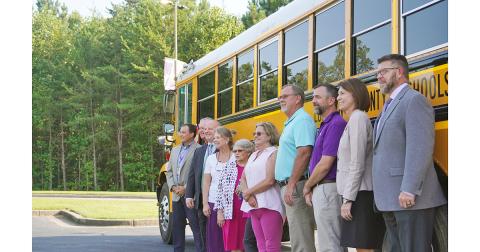 Members of the Board of Education and Central Office staff pose for a photo with one of the system's new buses.