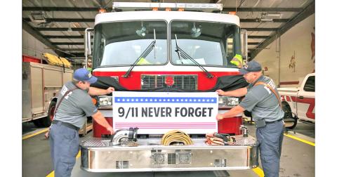 Firefighters/EMTs (from left) Jordan Dingess and Jody Holland from the Lumpkin County Fire Department check the fit of a banner that will be used for the 9/11 20th Anniversary Commemoration event on September 11, on the west end of the Gold Museum in downtown Dahlonega. The fire truck will be parked in front of Woody’s Barber Shop.