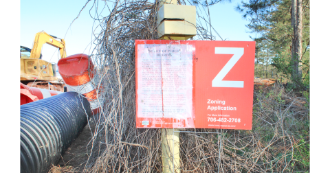 A sign advertising the March 7 meeting of the City Planning Commission stands at the end of Pinetree Way. Residents showed up to the hearing to express their skepticism of the project, which would include a 325-unit apartment complex and 10,000 feet of commercial space.