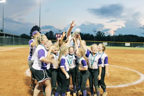The Lumpkin 10U softball team celebrates their state win as the sun sets over the field.