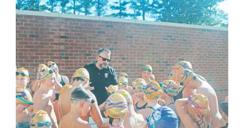 Lumpkin County Coach Jesse Turk leads the young swimmers in a chant before the team dove into the competition.