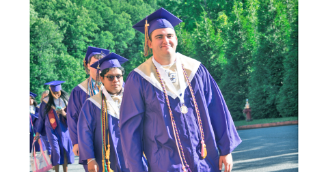 Senior member of the football team, Matthew Reece, smiles in his graduation cap and gown as he and his classmates prepare for commencement.