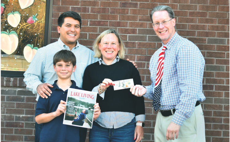 Jonathon, Sarah, and Jonathon Barge Jr., who goes by “J,” are all smiles having learned that Jonathon Barge won the Winter 2022 Lake Living cover contest for the picture of “J” in the family’s 1972 Alumacraft fishing boat “catching snowflakes instead of fish” on Lake Burton in January 2022. Enoch Autry, publisher of The Clayton Tribune in Rabun County, right, hands the family the $100 prize for winning the contest. (Photo by Megan Broome)