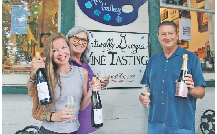 Naturally Georgia manager Amanda Holt (left) and owner Vickie Cooper show off bottles of their proprietary Dragonfly White, while Engelheim Vineyards owner Gary Engel displays his new sparkling Glitzern.