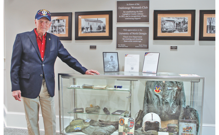 LTC Colonel (RET) Lewis “Lew” M. Houser is currently featured in a rotating exhibit at the Lumpkin County Library called “Outpost Alpha,” which honors local veterans. Here, he stands next to a glass case displaying Vietnam-era military memorabilia, including his Air Force flight jacket, helmet, gloves and service medals.