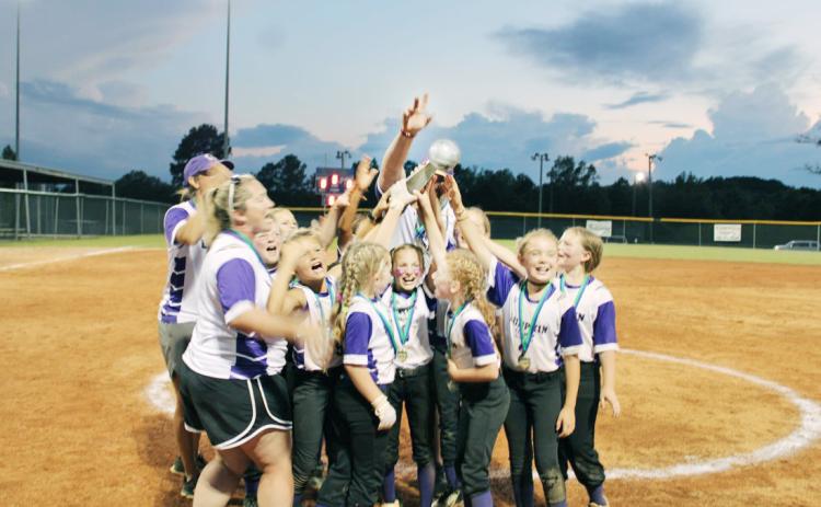 The Lumpkin 10U softball team celebrates their state win as the sun sets over the field.